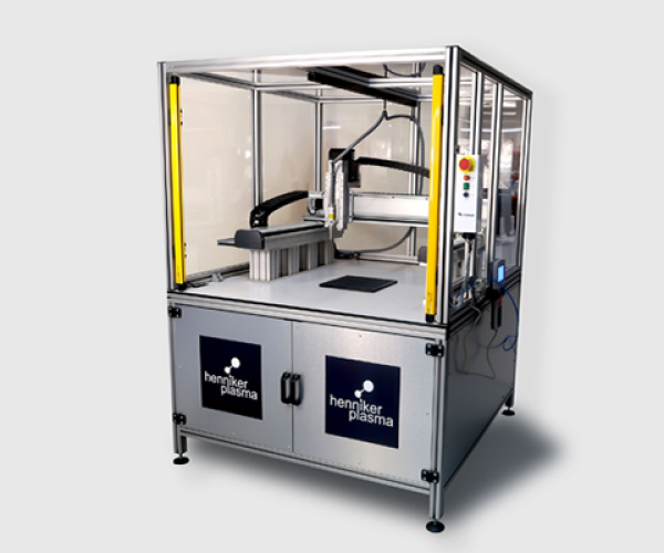 Automated atmospheric plasma system by Henniker Plasma designed for advanced surface prep, featuring an enclosed workstation with robotic arms for precise surface treatment in industrial and research applications.