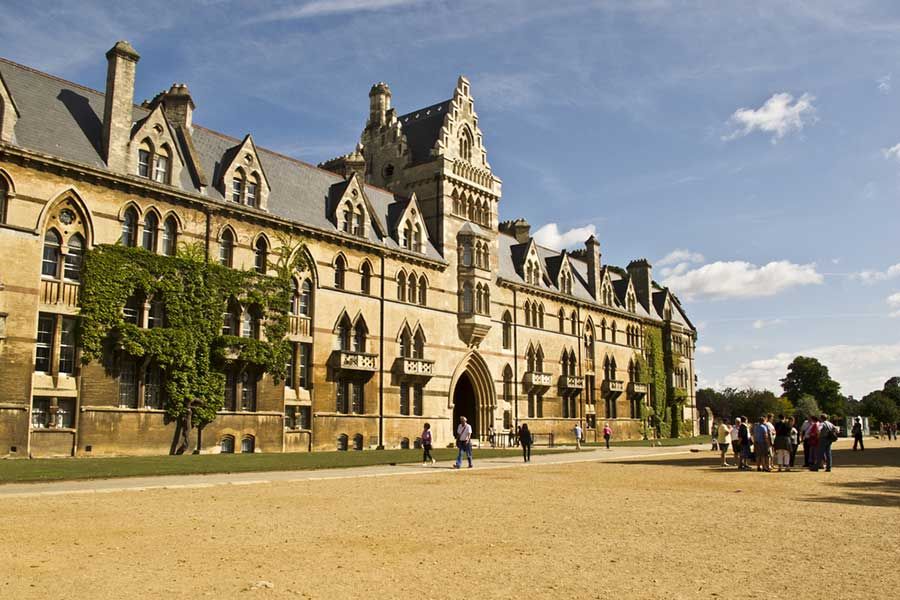 Historic university campus building with Gothic architecture and students walking in courtyard, UK higher education institution setting