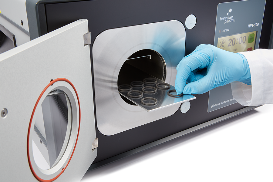 Technician placing samples into Henniker Plasma HPT-100 benchtop plasma treatment chamber for surface cleaning and activation in laboratory setting