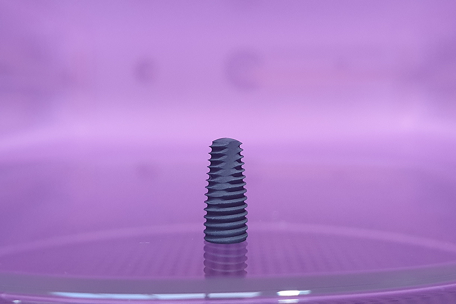 Medical implant screw undergoing vacuum plasma surface treatment to enhance biocompatibility and coating adhesion