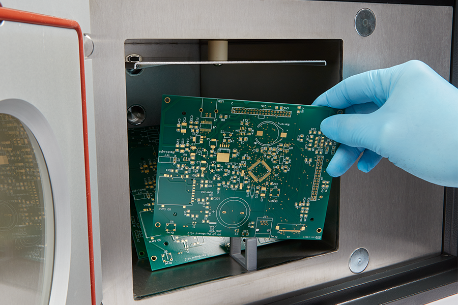 Printed circuit board (PCB) being placed into plasma treatment chamber for surface cleaning and improved soldering adhesion in electronics manufacturing